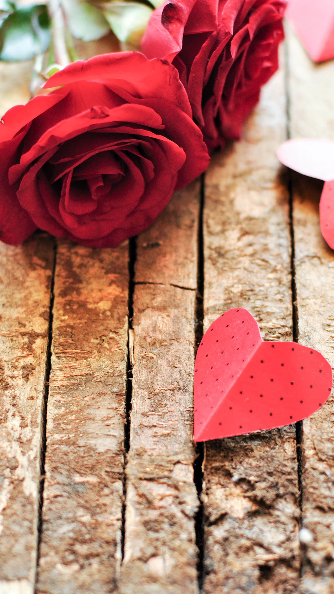 a red rose and a paper heart on a wooden table