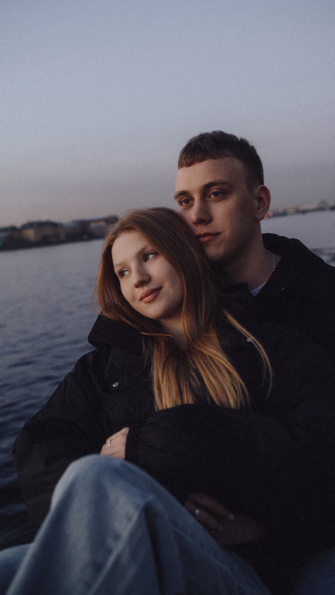A couple embraces by the water at dusk
