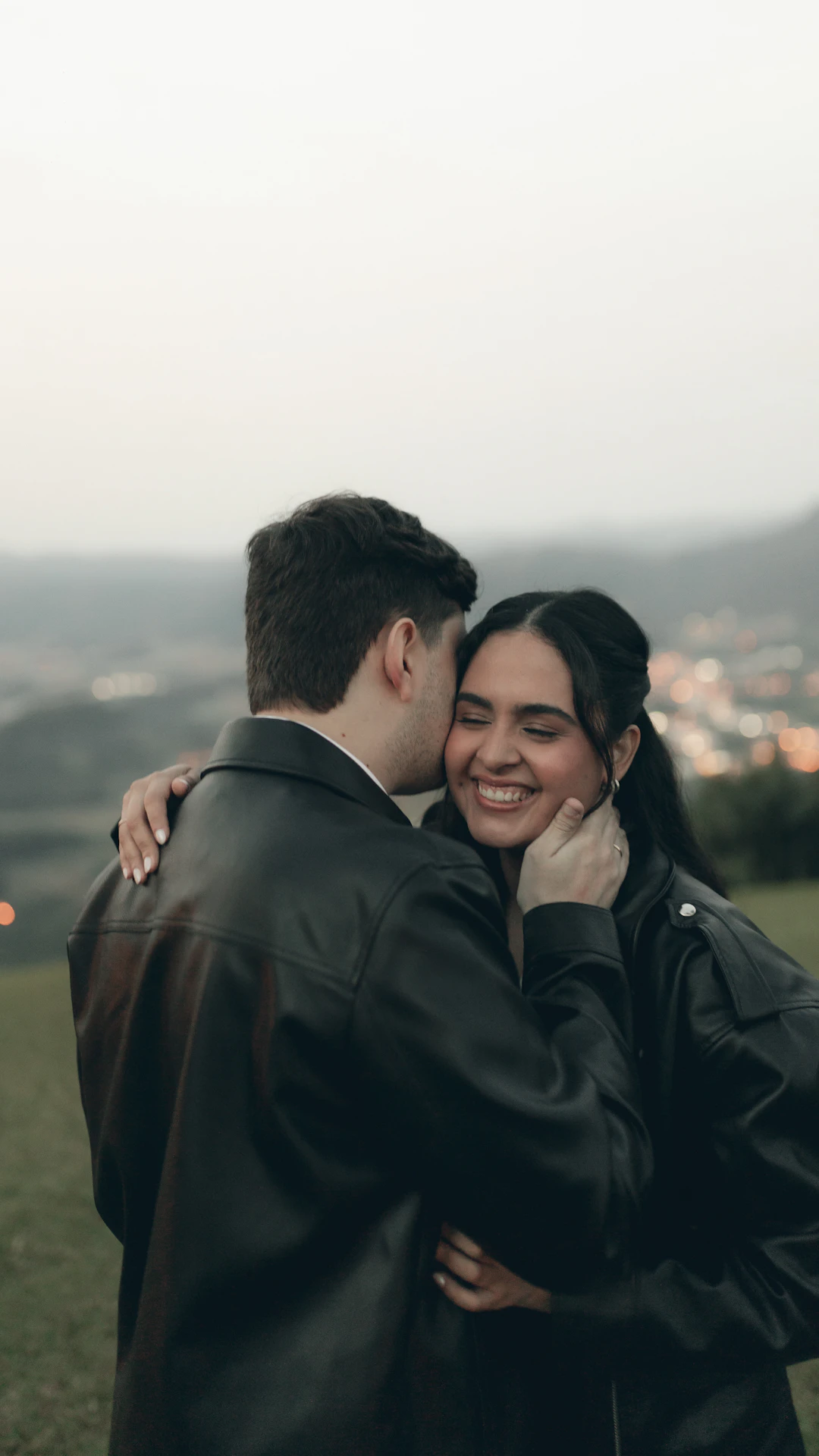 Couple embracing on a grassy hill at dusk