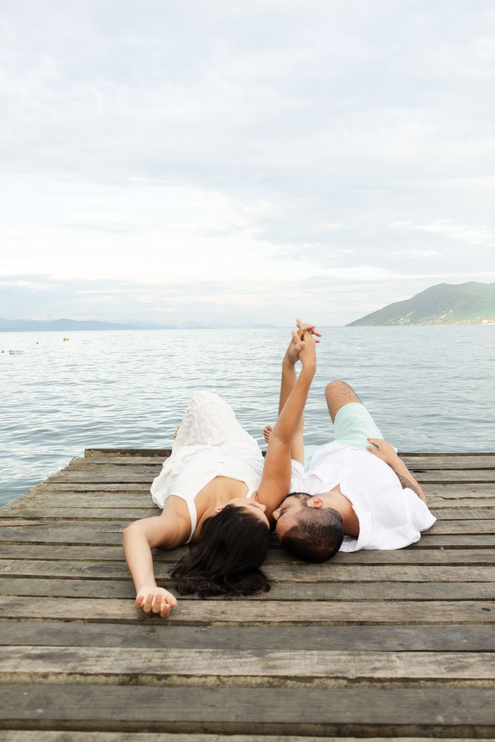 A couple lays on a wooden pier by the sea in São Paulo, enjoying a serene moment under a calm sky.