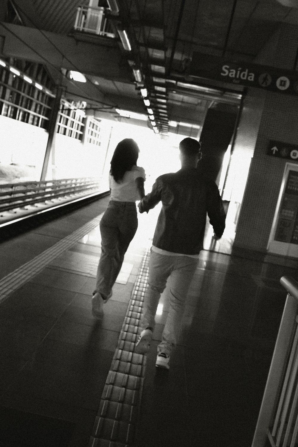 Man and woman running hand-in-hand on a railway platform in black and white.