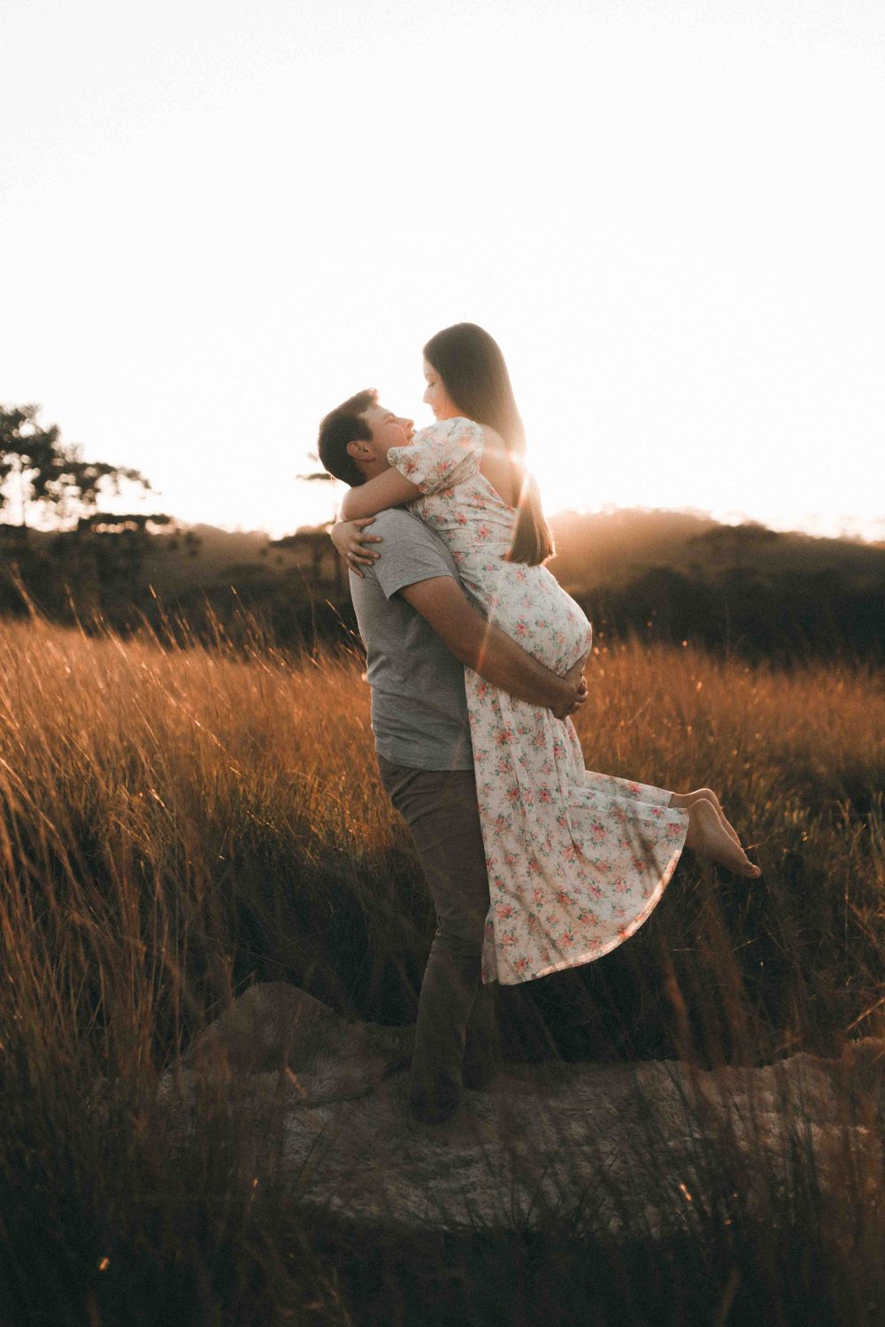 A romantic moment captured with a couple embracing in a sunlit field during sunset.