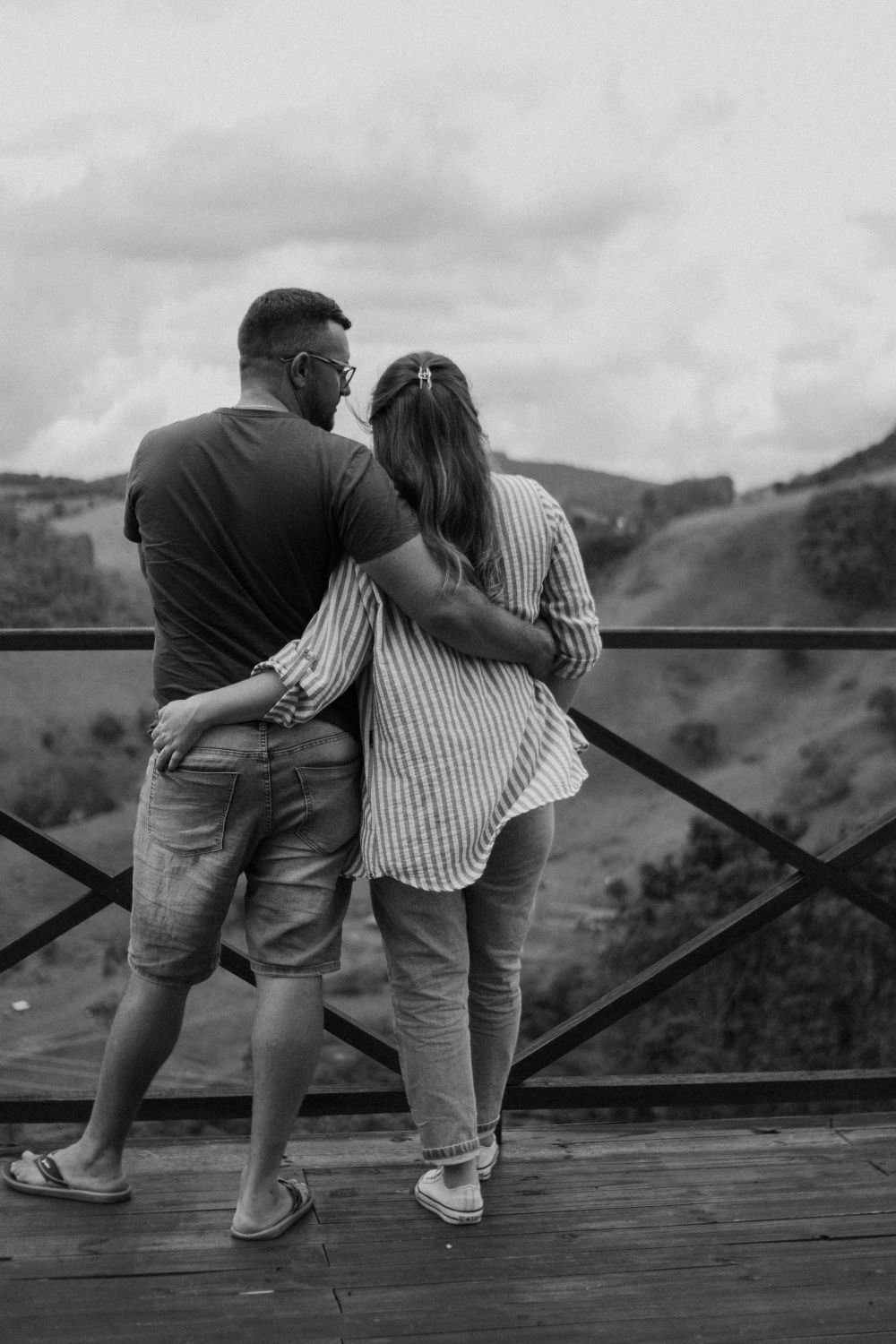 Black and white photo of a couple embracing with a scenic mountain backdrop.