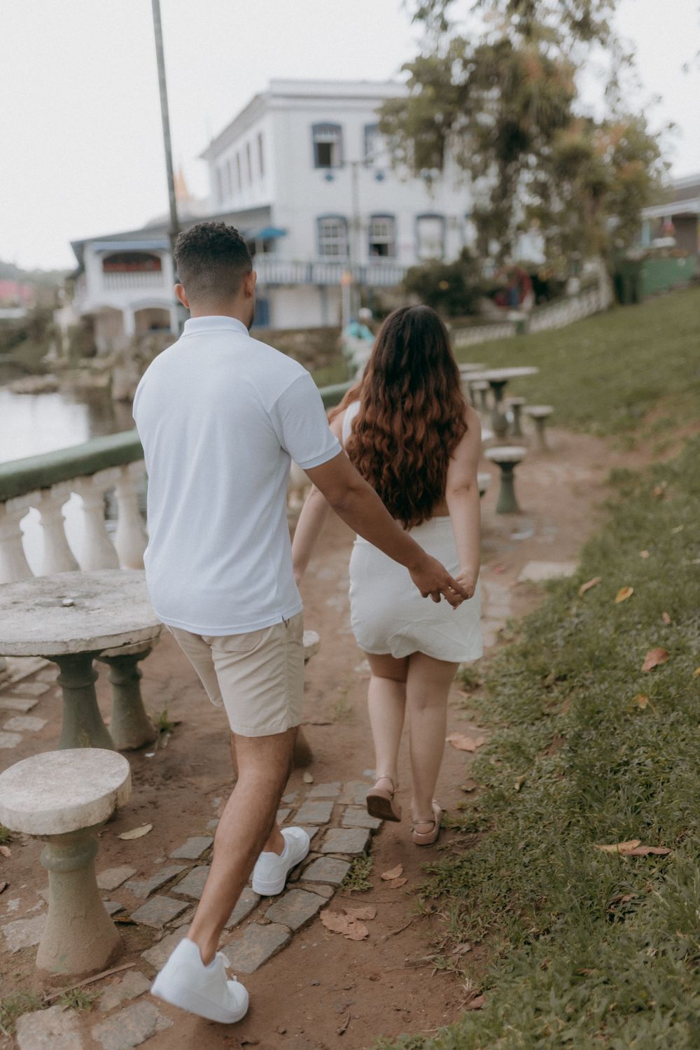 A couple walking hand-in-hand along a scenic river pathway near elegant architecture.