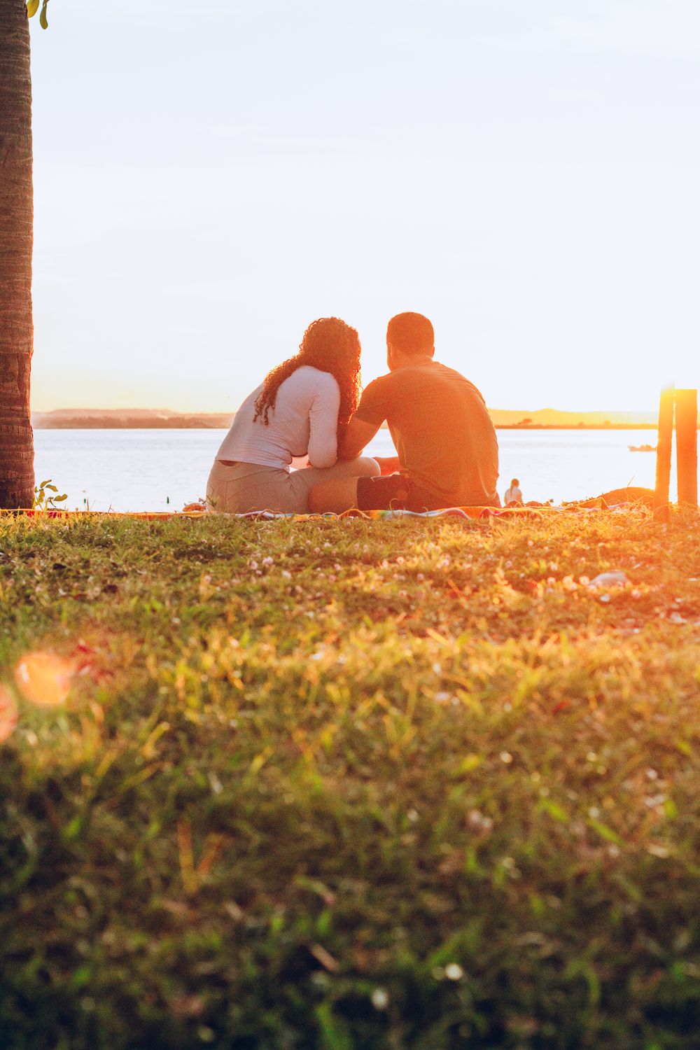 Couple sitting on grass beside ocean during sunset in Palmas, Brazil.