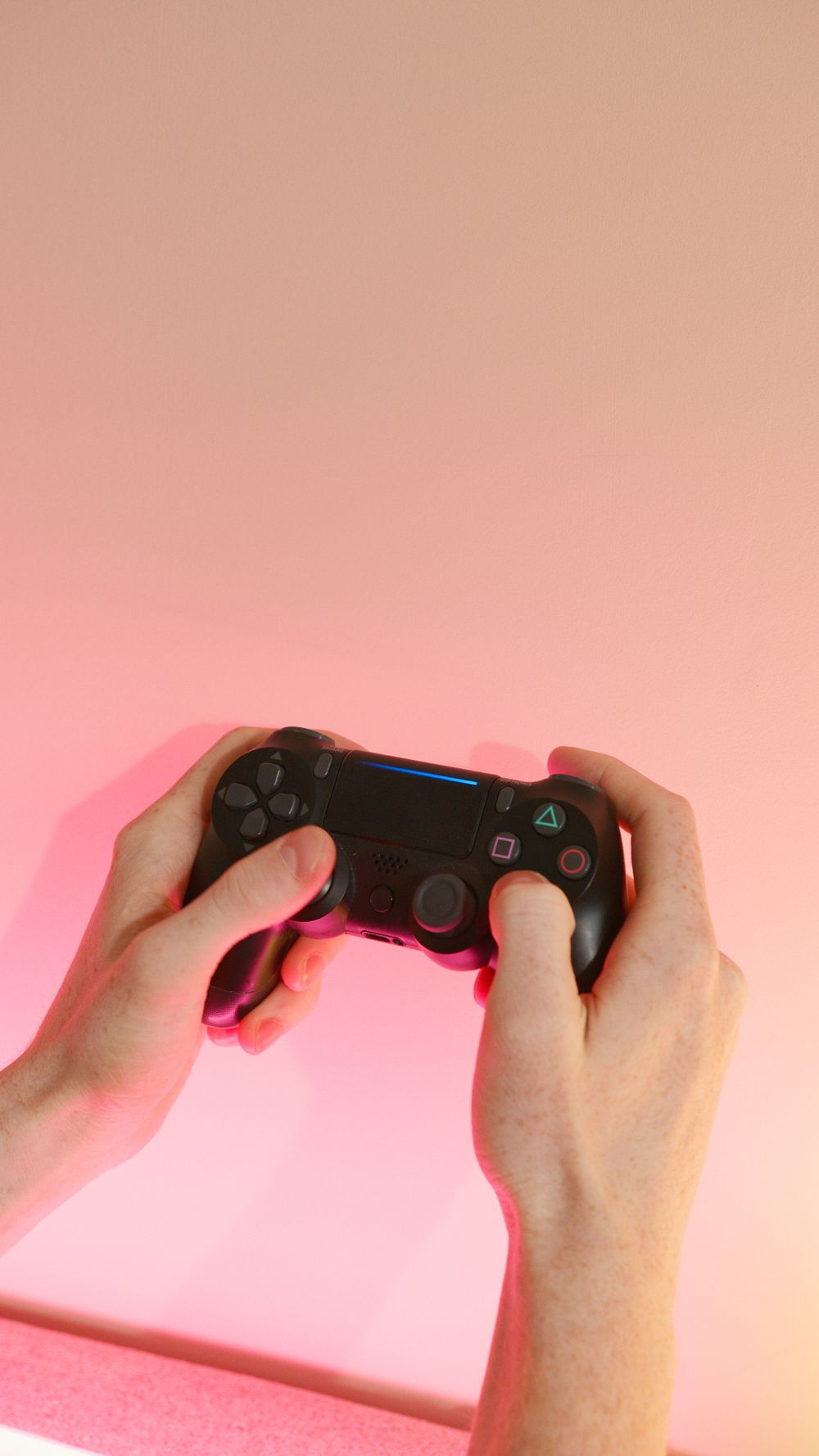 Person holding a wireless game controller with a pink background, showcasing gaming technology.